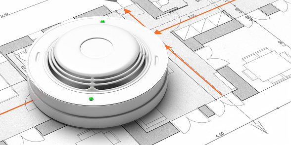 A close up shot of a fire alarm sitting on top of blueprints.