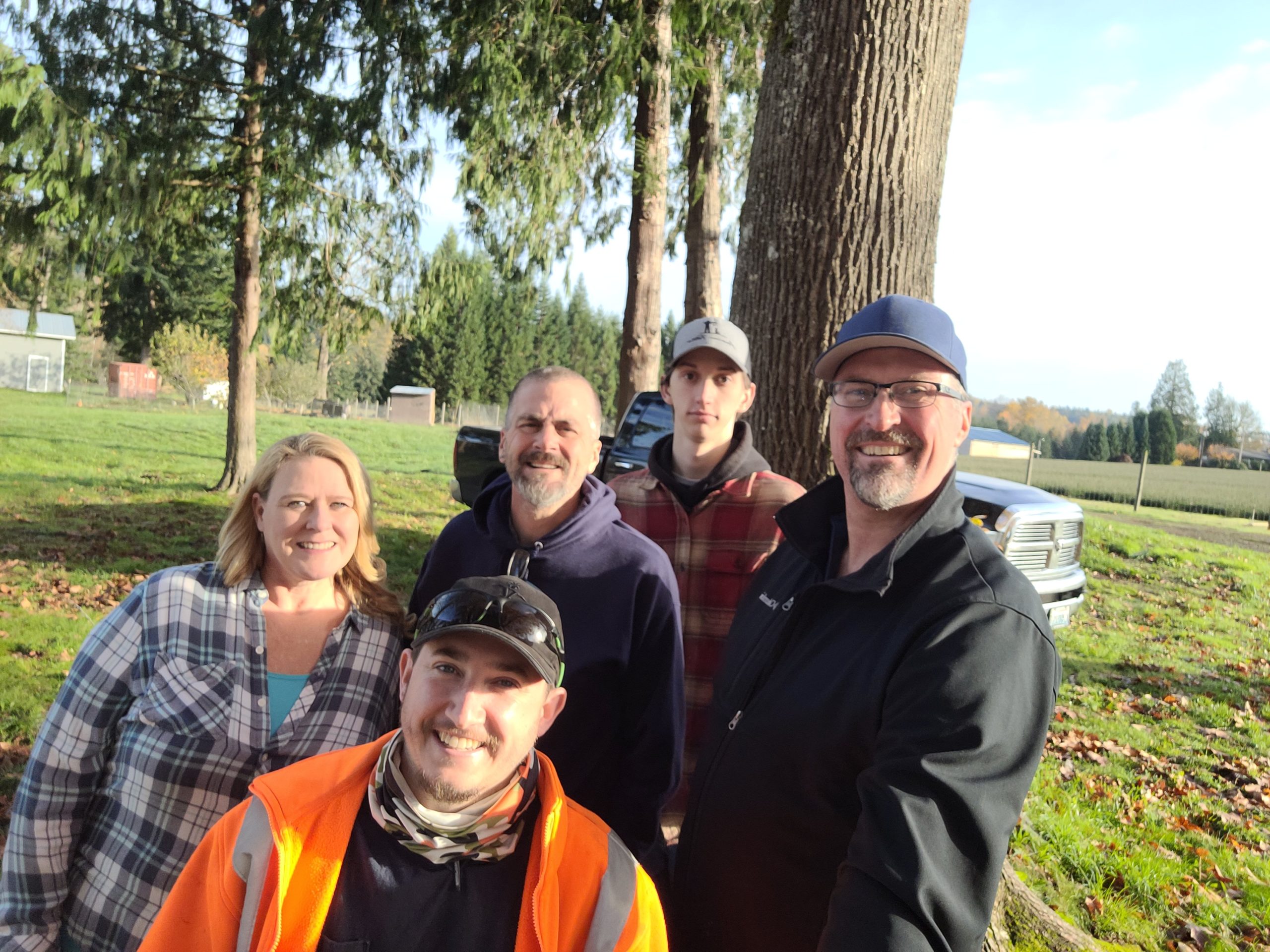 A group shot of 5 people smiling into the camera next to a few trees.